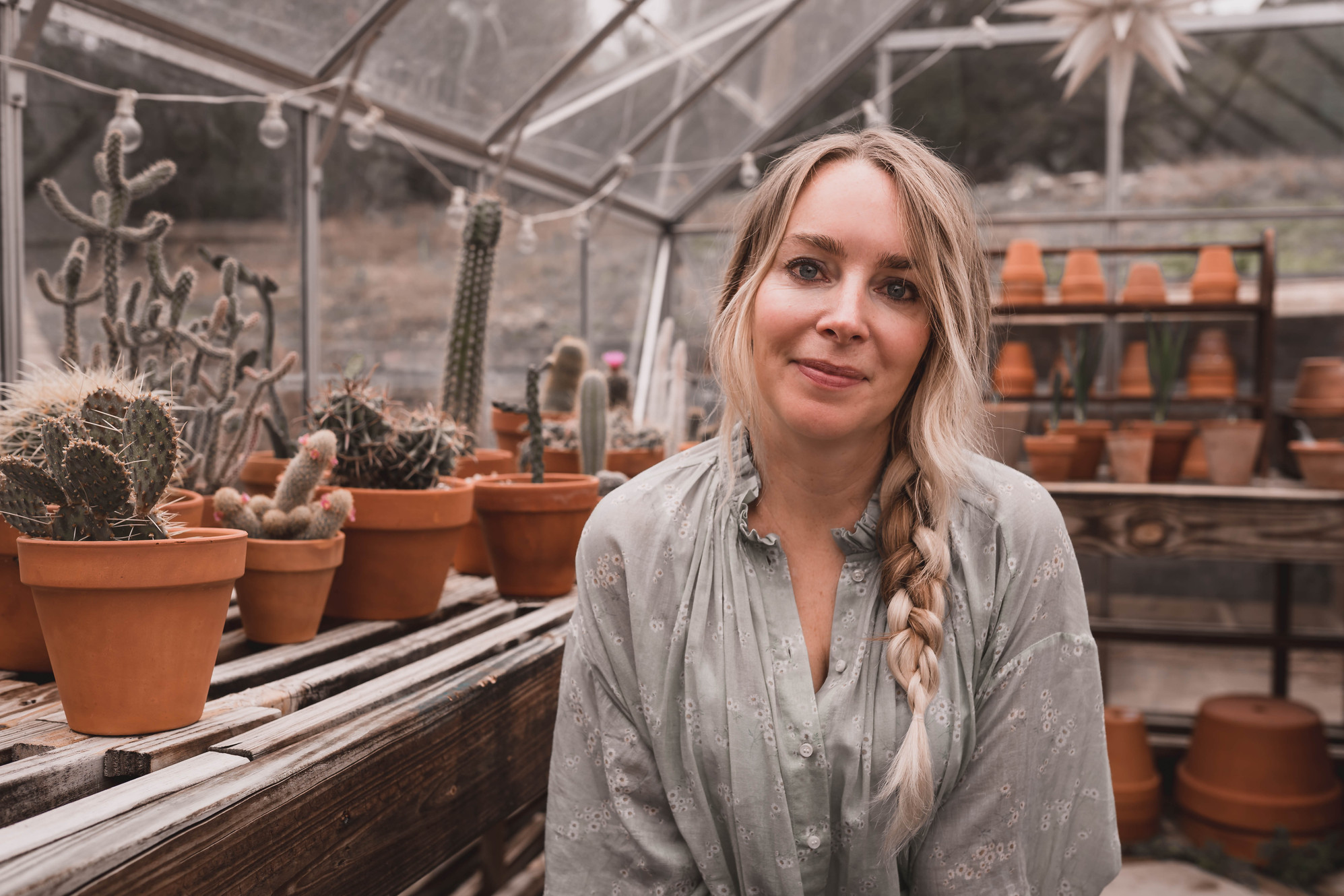 Sarah Fr&eacute;mont in the greenhouse, surrounded by potted cacti and terra-cotta